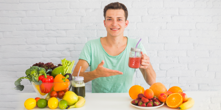 Man having a superfood drink with various healthy vegetables and fruits present on the table.