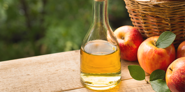 A flask of apple cider vinegar with apples in the background.