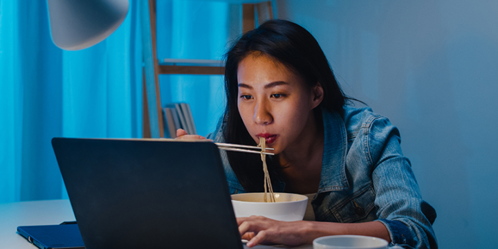Woman eating noodles at night while watching something on the laptop